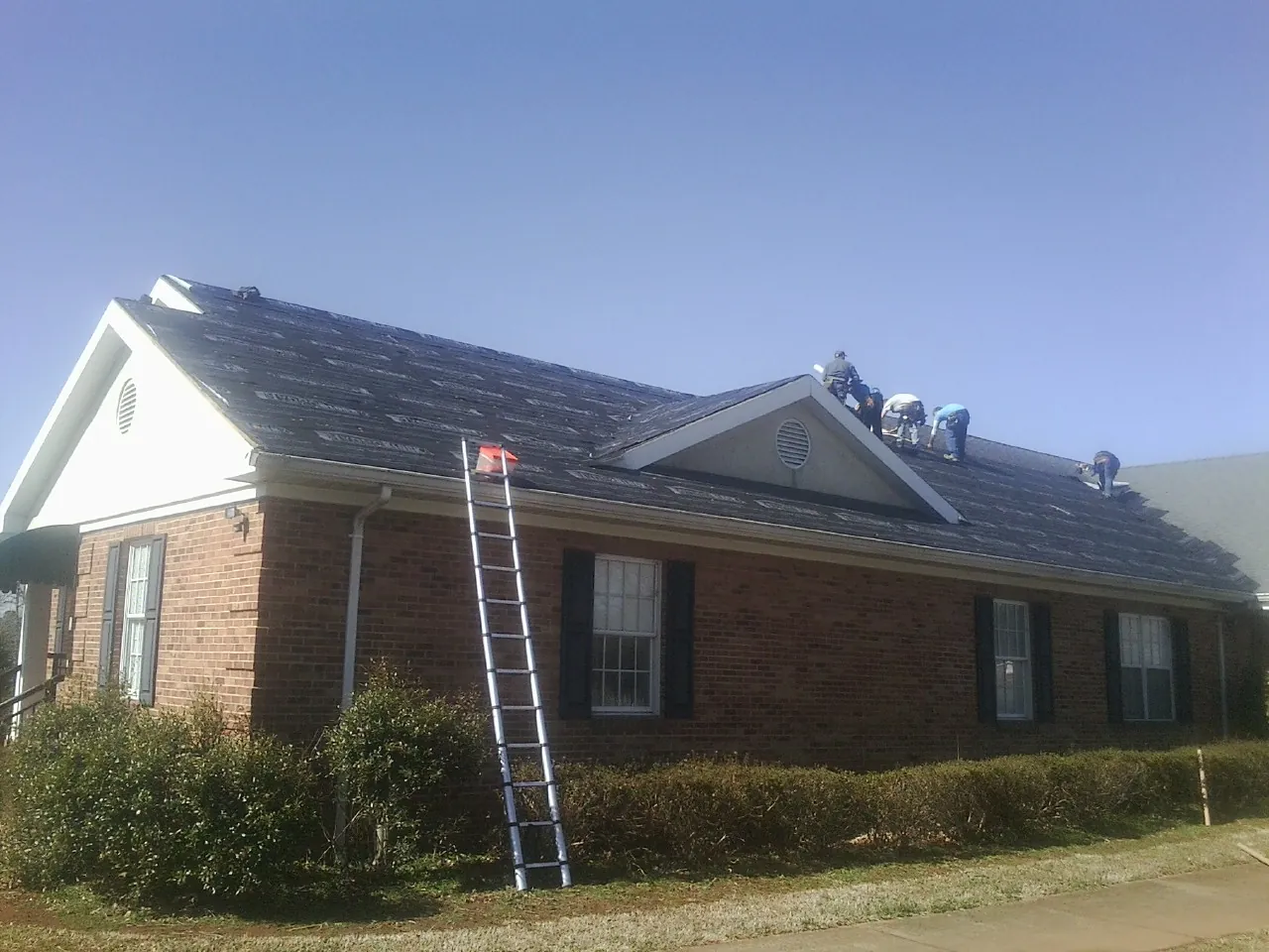 Crew tearing shingles off a brick ranch roof with a ladder set — Metal Roof Repair work by our crew in Hartselle