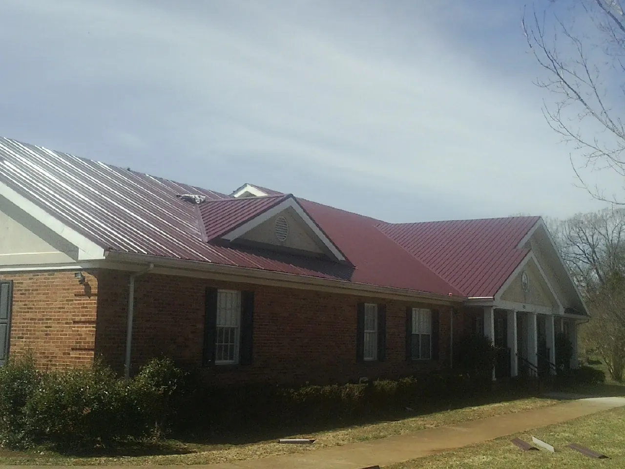 Red metal roof with gabled entries on a long brick building, from a Hail Damage Roof Repair job in Hartselle