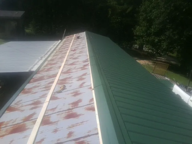 Old rusted panels beside newly installed green metal roofing — Wind Damage Roof Repair by Roofing Brothers in Hartselle