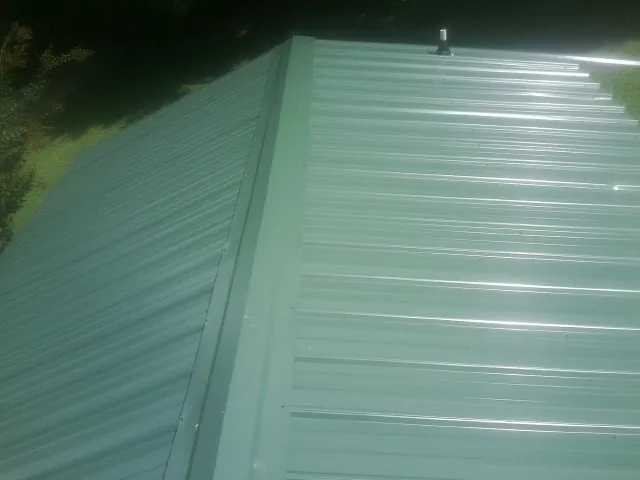 New green metal panels meeting at the ridge of a roof — Flat Roof Repair work by our crew in Hartselle