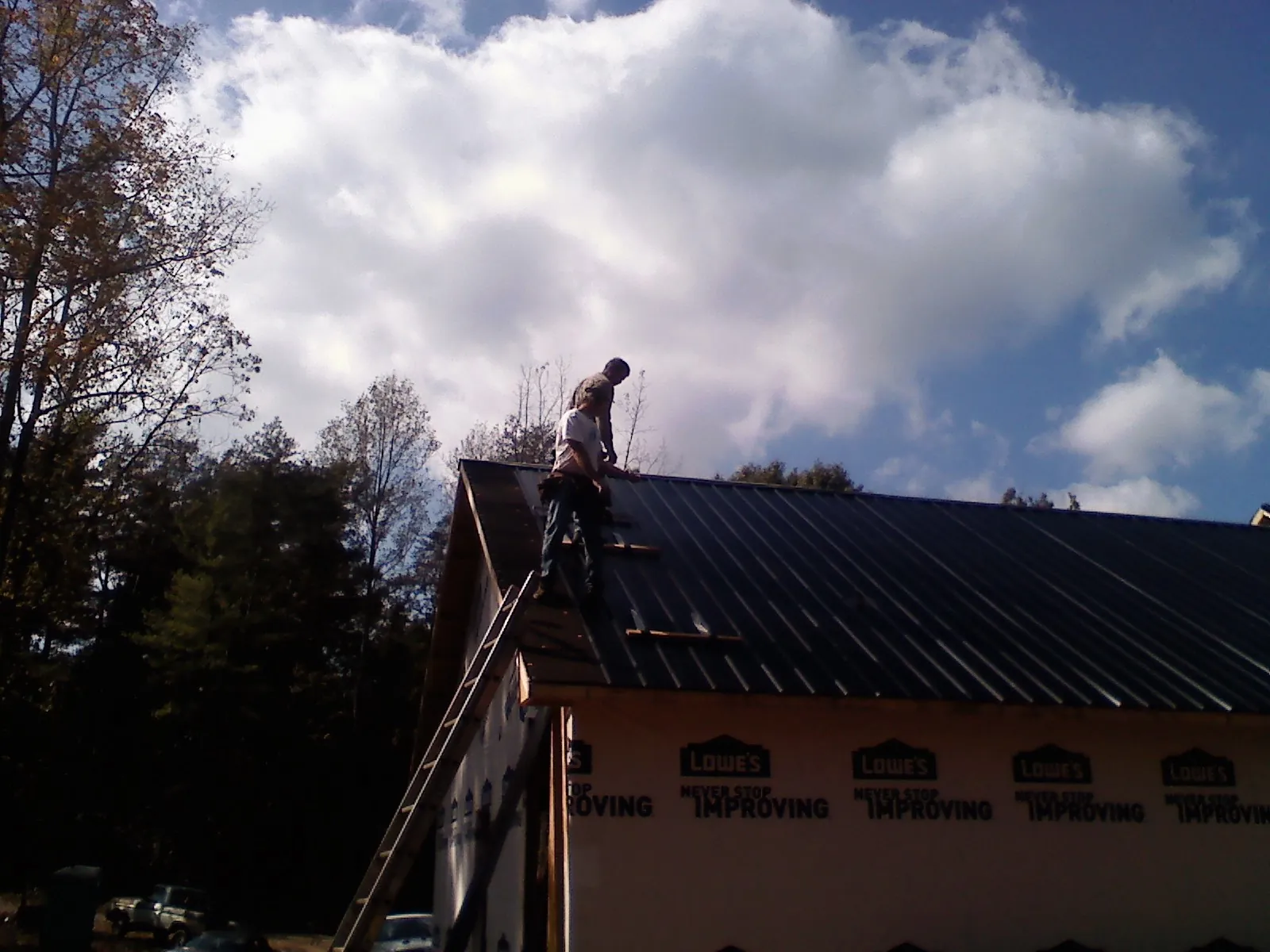 Roofer fastening dark metal panels high against a cloudy sky, from a Roof Inspection job in Hartselle