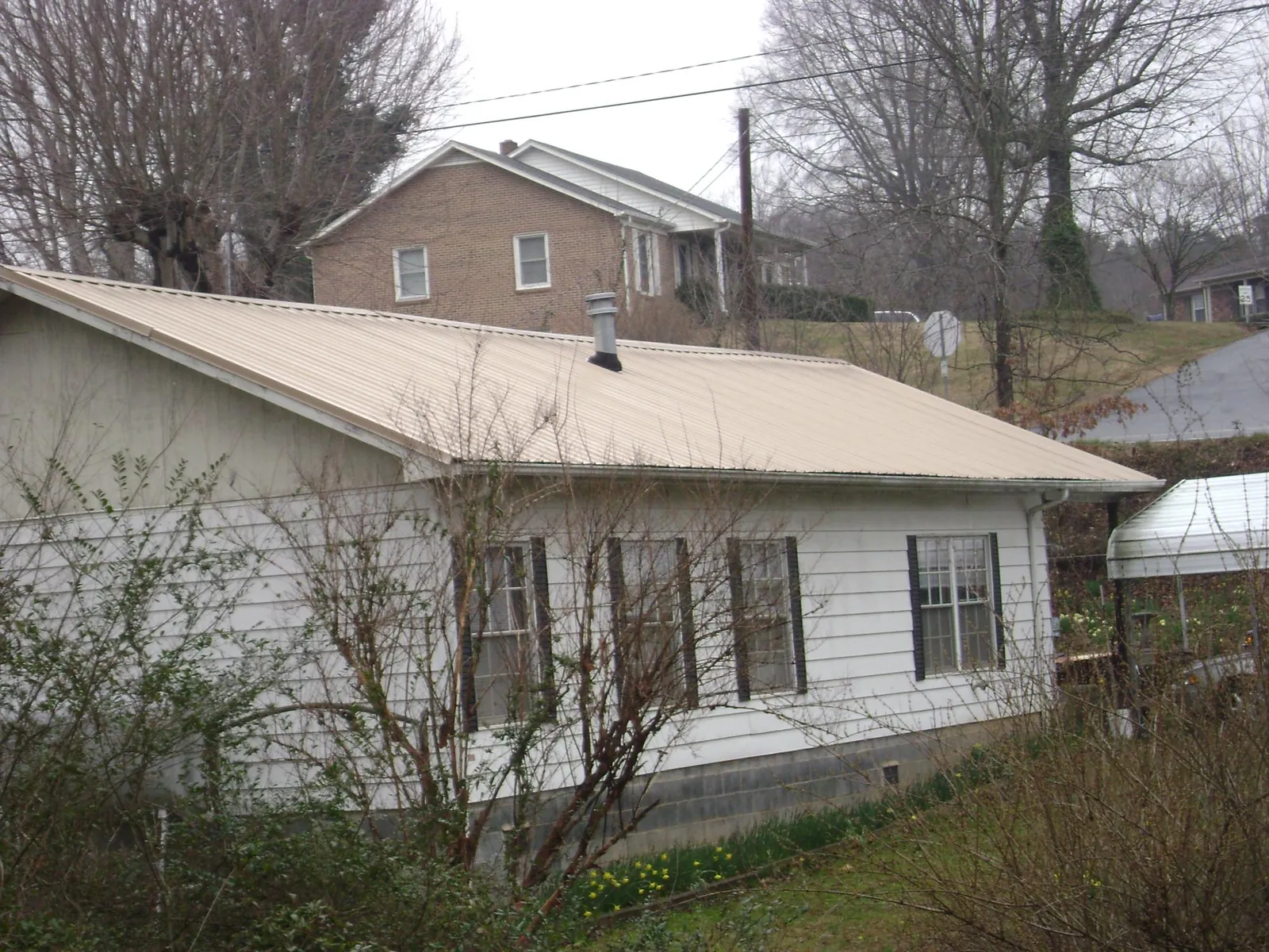 Tan metal roof on a white sided house set into a hillside — Commercial Roofing by Roofing Brothers in Hartselle