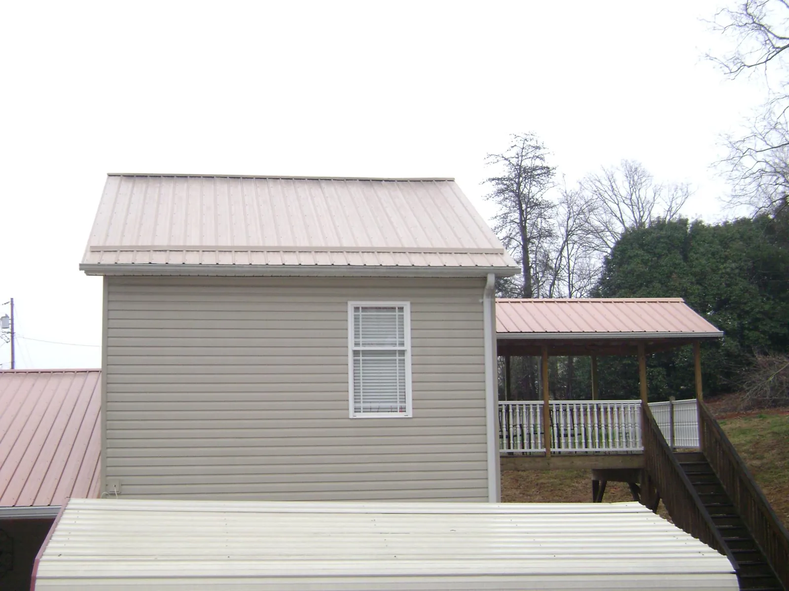 Tan metal roofs on a two story addition and attached porch, from a Roof Replacement job in Hartselle